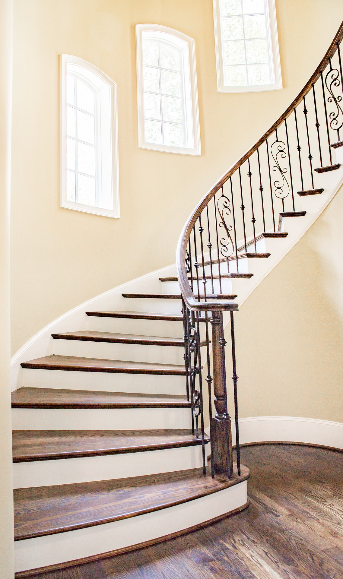 "Custom curved staircase railing installation featuring decorative wrought iron balusters and elegant interior stair design."